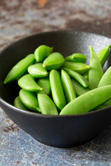 Sugar snaps in a black stone dish bowl.  On a grunge background