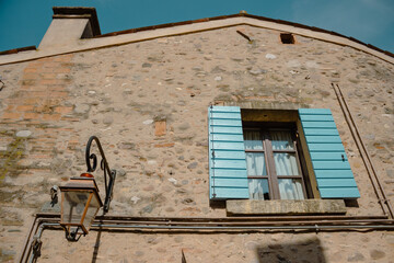 Fototapeta na wymiar Detail of an old building with a blue shuttered window and a lamppost hanging on the wall. Borghetto sul Mincio, Italy.