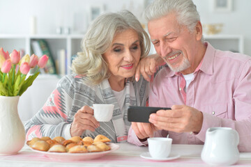 Portrait of happy senior couple with smartphone drinking tea