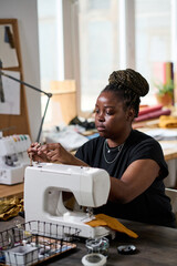 Young creative African American female clothes designer sewing new attire for clients or fashion...