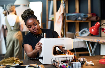 Young serious black woman in casualwear sewing new fashionable attire for clients of her boutique...