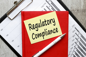 text on a yellow sticky note on a folder with financial charts REGULATORY COMPLIANCE