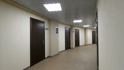 Empty, round corridor with light beige walls and closed, dark brown doors. Closed doors along a...