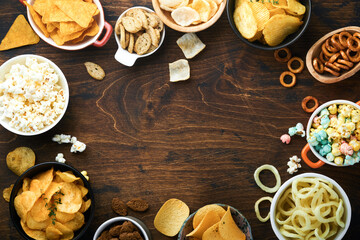 Unhealthy food or snacks. All classic potato snacks with peanuts, popcorn and onion rings and salted pretzels in bowl plates on old wooden background. Unhealthy food for figure, heart, skin, teeth.