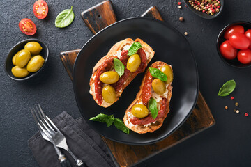 Bruschetta with sun dried tomatoes. Toast or sandwich with ricotta, sun dried tomatoes and Provence herbs with basil servered on black plate on black background table. Top view banner menu recipe.