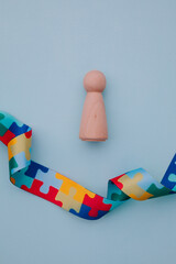 World Autism awareness and pride day with puzzle pattern ribbon and wooden model of person on a blue background. Vertical image