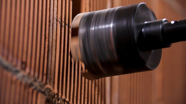 Close up of male with electric drill perforator before making a hole in red brick wall. Stock footage. Worker and professional tool at the construction site.