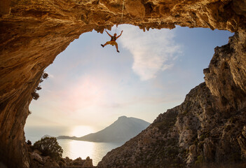 Female rock climber hanging on rope while lead climbing in cave with beautiful sea view