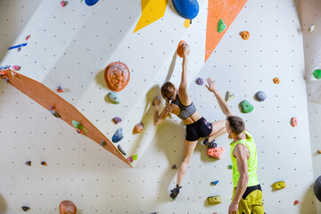 Rock climbers in climbing gym. Young woman climbing bouldering problem, man giving her instructions.