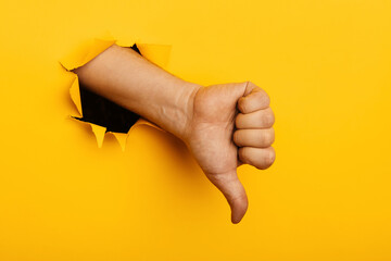 Hand shows a thumb down through a hole of yellow paper wall