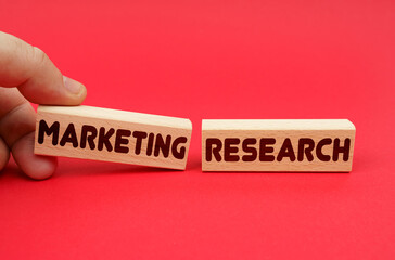 On a red background, wooden blocks, one of them in hand. The blocks are written - MARKETING RESEARCH