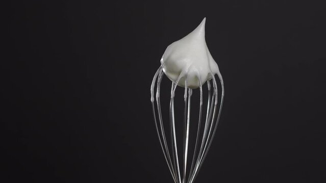 Metal whisk with whipped egg whites, isolated on black background, close up, rotates