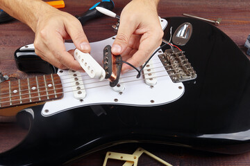 Guitar repairman selects pickup for replacement on electric guitar. - obrazy, fototapety, plakaty