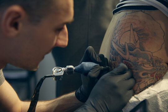 The master creates a picture on the body of a young beautiful girl. Close-up of hands and tattoo machine