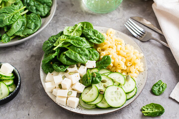 Bowl with pasta, cucumber, cheese and spinach on the table. Healthy vitamin nutrition. Close-up