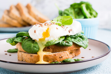 Appetizing sandwich with poached egg, spinach and flax seeds on a plate. Flexetarian Diet. Close-up