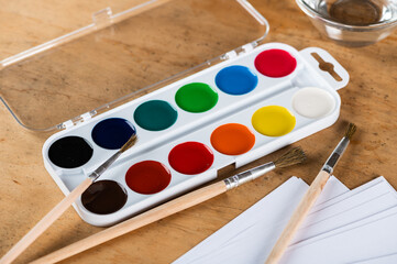 paintbrushes palette and watercolor paints with white paper. Artist workplace