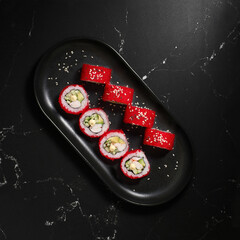 Traditional delicious fresh sushi roll set on a black background. Sushi roll with rice, nori, cream cheese, tobiko caviar, avocado. Sushi menu.