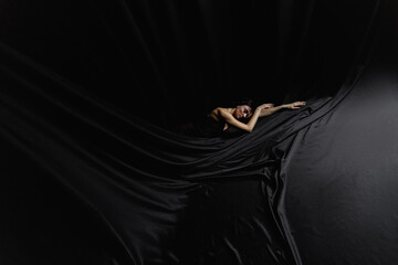  ballerina lies on a black satin fabric © Anton
