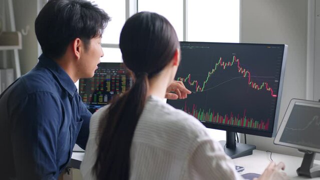 Young Asian investors analyzing about stock market and cryptocurrency investment from graph in computer laptop together.