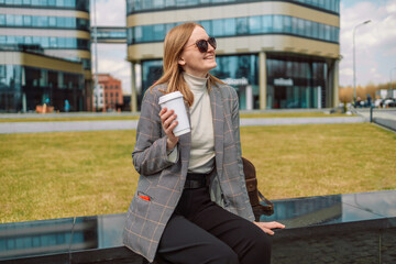 Woman holds a eco paper cup with coffee or tea and walks in spring park. Drink coffee time....