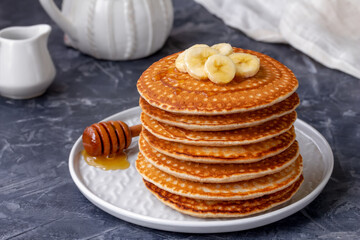Stack of pancakes with slices of fresh bananas and honey on top. Horizontal. 