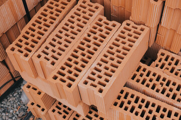 Red perforated bricks with rectangular holes on wooden pallets in an open-air warehouse ready for...