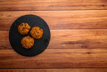 Cookies with pieces of chocolate on dark slate plate, light wood background. Top view, flat lay, space for text.