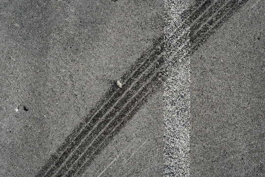 Asphalt texture with white line and tire marks. Smooth asphalt road. Tarmac dark grey grainy road background.Top view