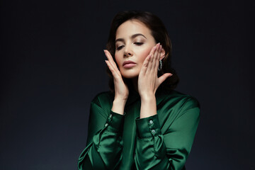 Self care. Elegant woman with curly hair wearing a green silk blouse touching her face