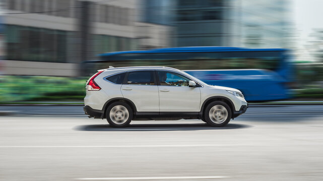 panning shot of white car Honda CRV driving on city road. Side view of SUV in motion with blurred urban background