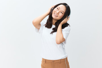 Naklejka premium Dreaming happy cute Asian young female in white basic t-shirt touch headphones looks aside posing isolated on over white studio background. The best offer for ad. Favorite Music App Ad concept
