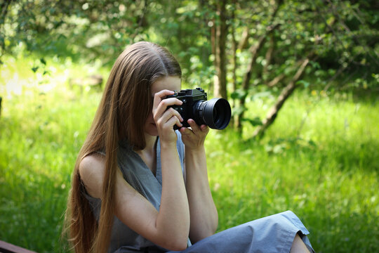 Long-haired Ukrainian woman takes pictures on a film camera of landscapes in a green park on a warm May day.