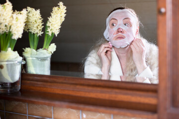 a middle-aged woman is busy with morning hygiene, she makes the face mask 