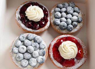 different pastries in a box, fresh cakes with berries and whipped cream, 