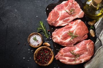 Raw meat. Fresh steaks with herbs, spices and vegetables at black background. Pork meat. Top view.