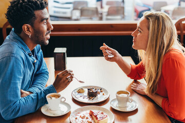 interracial couple having coffee and cake sitting at a table in a coffee shop