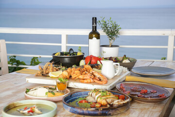 Table full of seafood and vegetable dishes with sea horizone in the background