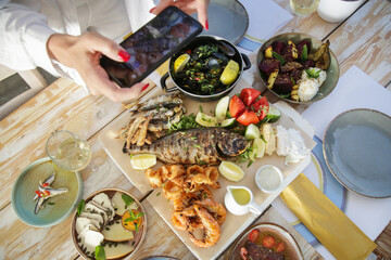 Woman using smartphone to take photos of food before eating in restaurant	