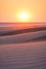 Sand dunes and seashore during sunset. Summer landscape in the desert. Hot weather. Lines in the sand. Landscape without people.