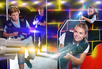 Excited children and theirs parents aiming laser guns at other players during lasertag game in dark room.