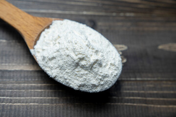 Whole flour in spoon on dark vintage wooden background. Close up view. Preparations for homemade baking. Basic ingredients for baking. 
Wheat flour on wooden spoon. 