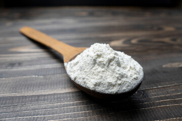 Whole flour in spoon on dark vintage wooden background. Close up view. Preparations for homemade baking. Basic ingredients for baking. 
Wheat flour on wooden spoon. 