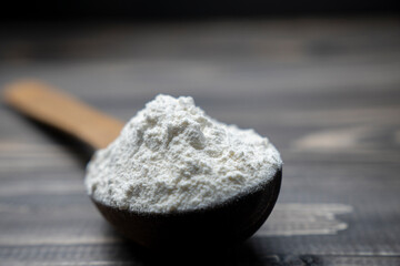 Whole flour in spoon on dark vintage wooden background. Close up view. Preparations for homemade baking. Basic ingredients for baking. 
Wheat flour on wooden spoon. 
