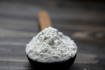 Whole flour in spoon on dark vintage wooden background. Close up view. Preparations for homemade baking. Basic ingredients for baking. 
Wheat flour on wooden spoon. 
