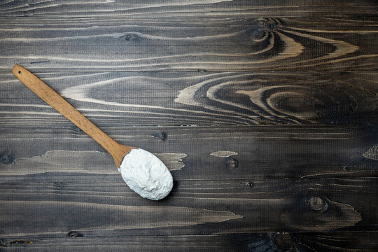 Whole flour in spoon on dark vintage wooden background. Close up view. Preparations for homemade baking. Basic ingredients for baking. 
Wheat flour on wooden spoon. 