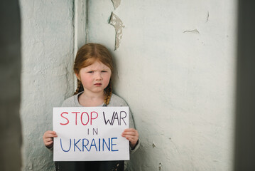 Upset poor toddler girl kid protesting war conflict raises banner with inscription text Stop war in...
