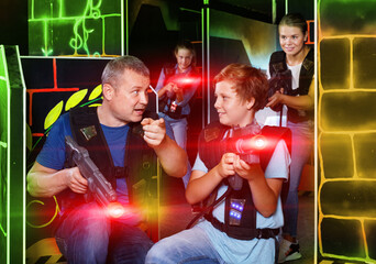 Happy glad cheerful positive teen boy with laser gun having fun on lasertag arena with his father