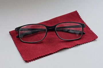 one black glasses lies on a red scarf on a white table