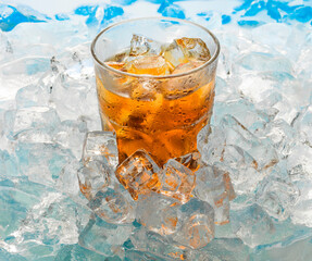 
a misted glass with a chilled brown-gold drink and ice cubes stand in the ice